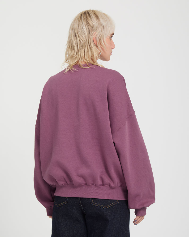 A person viewed from behind wearing a loose-fitting, heavyweight purple Volcom Sto N Crew sweatshirt with ribbed cuffs and hem.