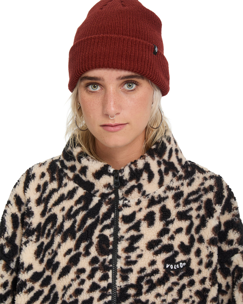 A person wearing a maroon beanie and a Volcom Wylding Out Sherpa, an oversized leopard print sherpa jacket.