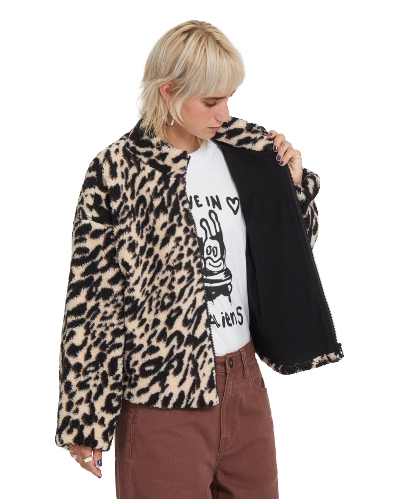A person wearing a Volcom Wylding Out Sherpa, an oversized leopard print jacket with a black lining, over a white graphic t-shirt and brown pants.