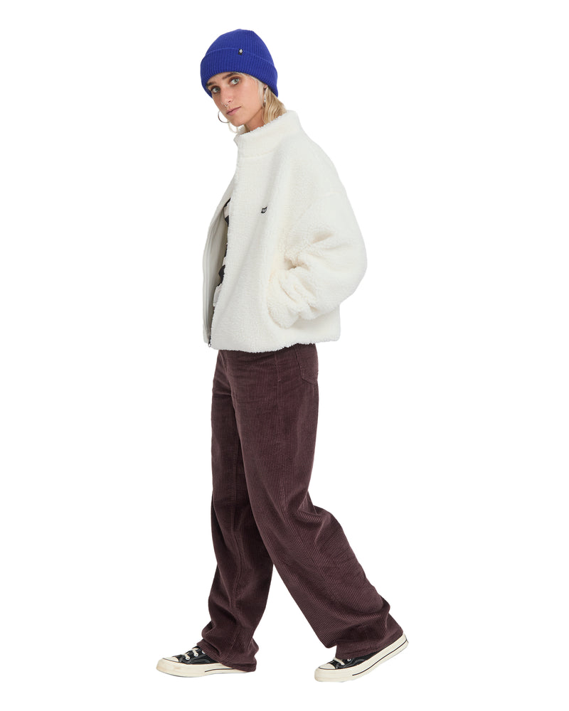 A person wearing a Volcom Women’s Wylding Out Sherpa jacket, a blue beanie, and brown corduroy pants.