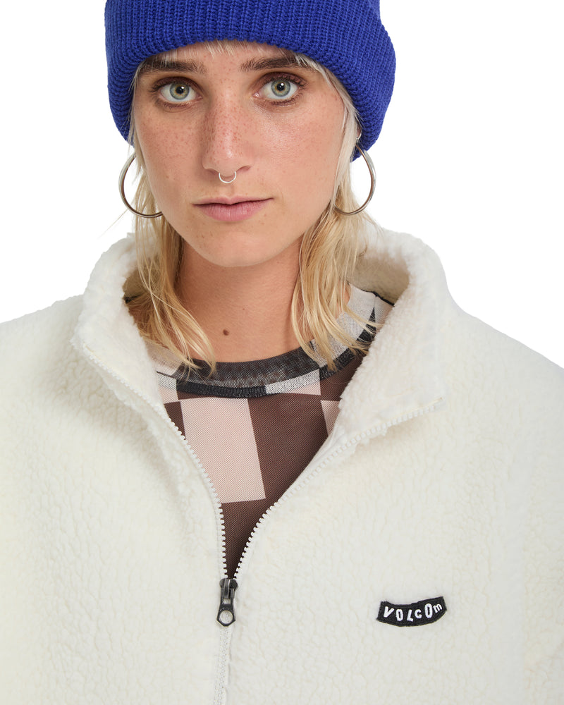 A person wearing a blue beanie and an oversized white, zip-up Volcom Women’s Wylding Out Sherpa jacket featuring a small black logo patch on the chest.