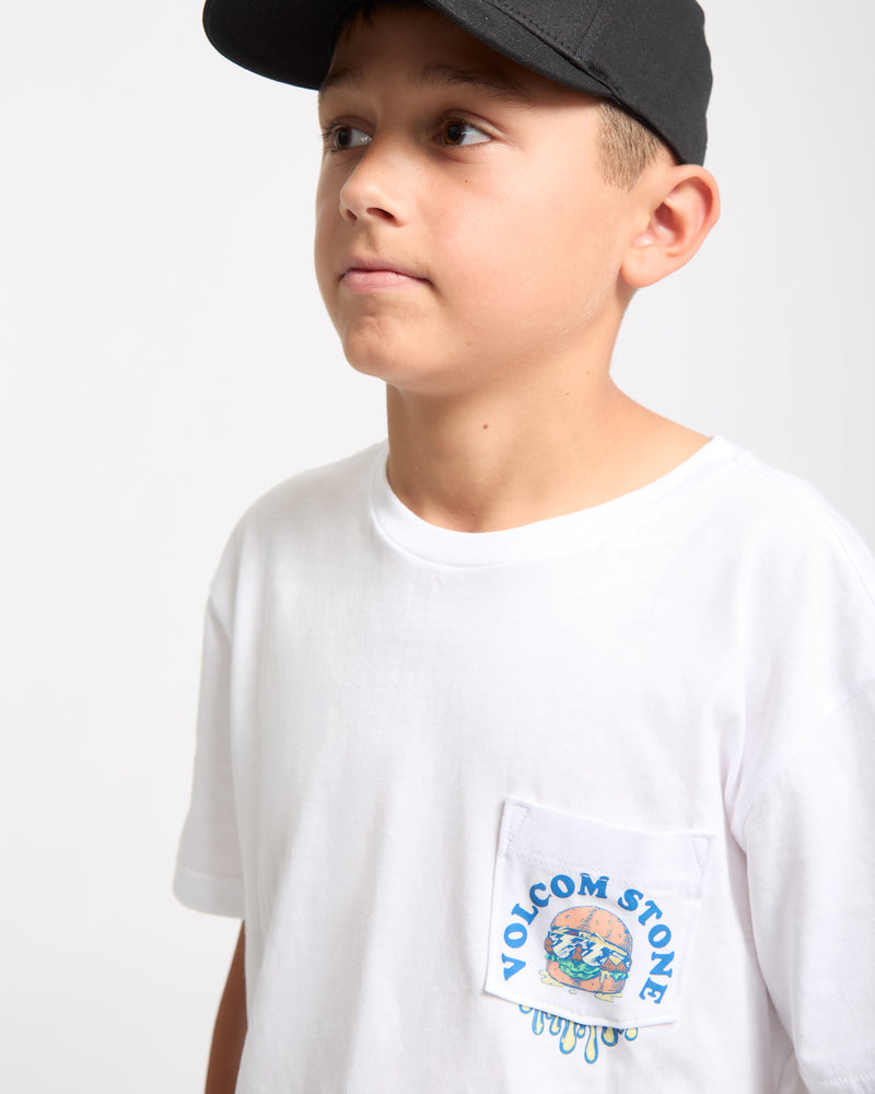 A boy wears the Kids' Burgstone Pocket Tee—a white shirt with a small Volcom Stone logo and colorful chest pocket art—and a black cap, looking slightly upward against a plain background.