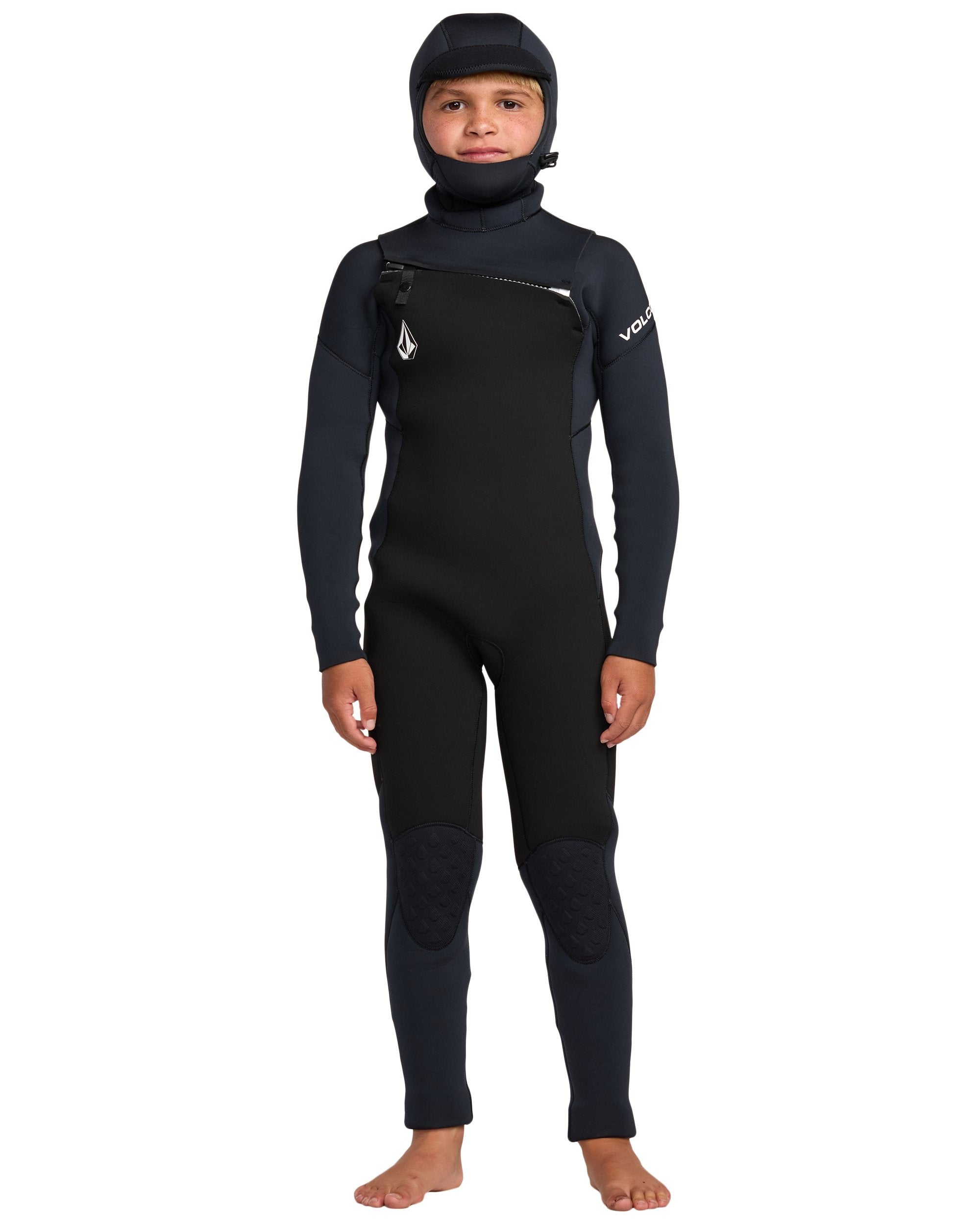 A child wears the Volcom Kids' 5/4 Mm Hooded Chest Zip Long Sleeve Full Wetsuit, featuring a front chest zipper, hood, reinforced knee pads, and Volcom branding on the chest and sleeve.
