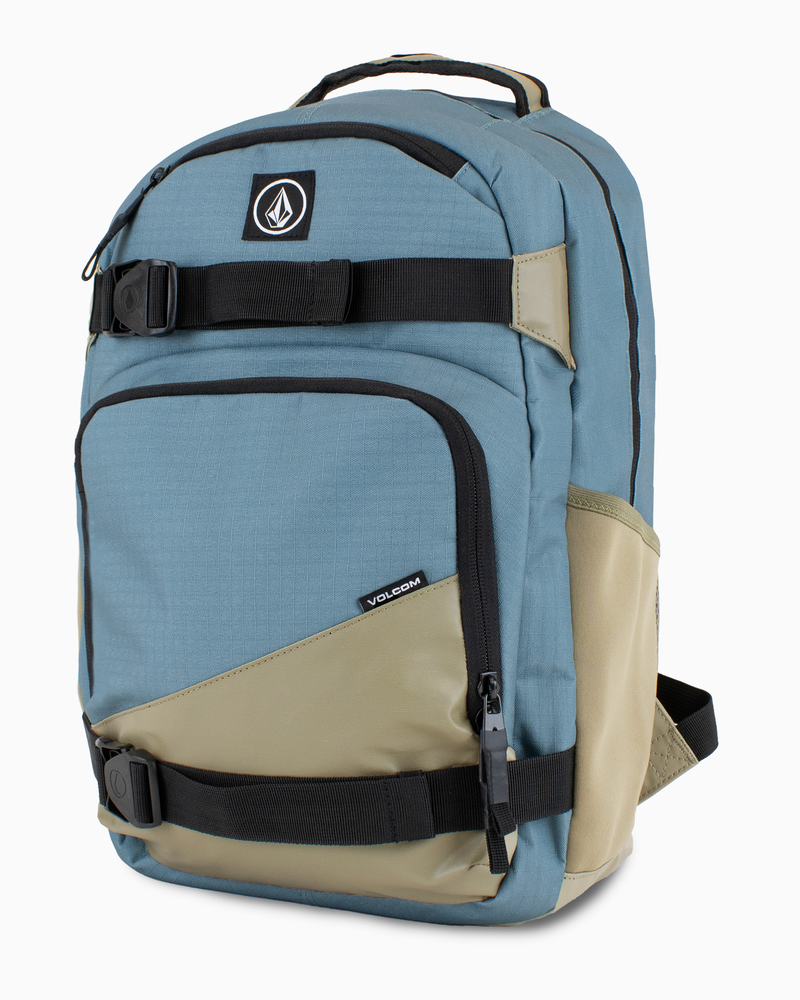 The Volcom Men's Grindstone Skate Backpack features a blue and khaki design with black ergonomic straps, front zippered pockets, a padded laptop sleeve, and a Volcom logo patch on the top pocket.
