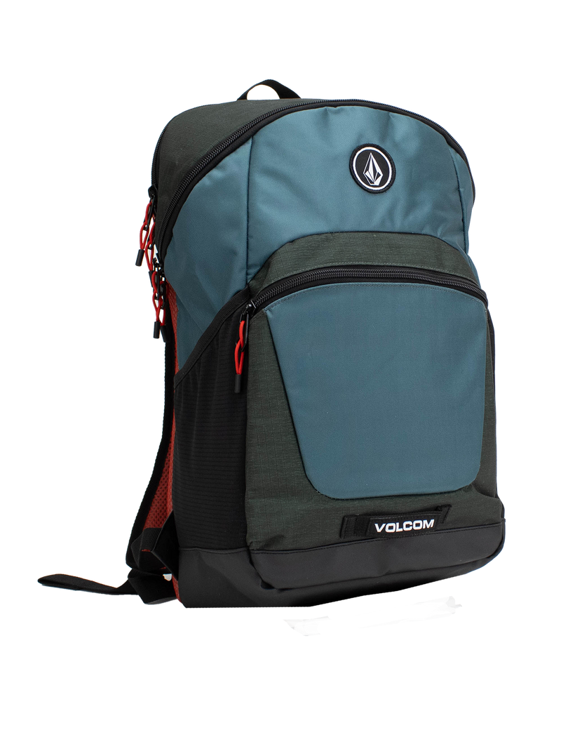 The Volcom Men's Slam School Backpack, shown in blue and black with red zipper pulls, features a front zip pocket, a large main compartment with a padded laptop sleeve, and a side mesh pocket, displayed standing upright on a white background.