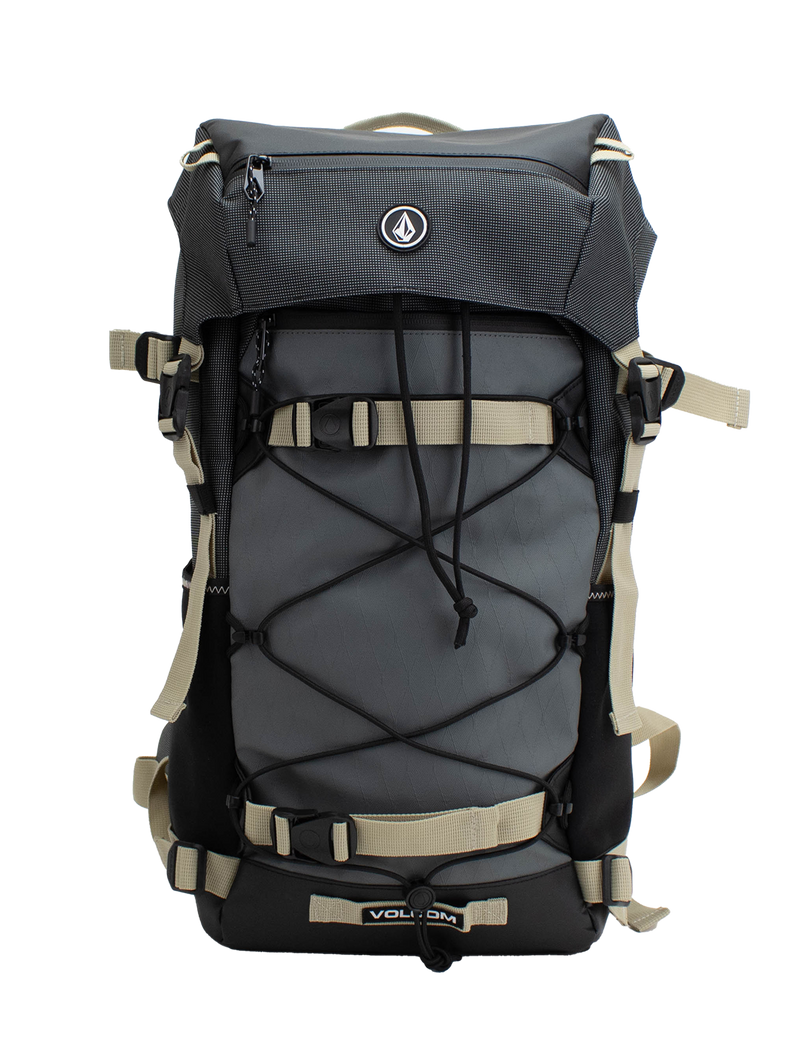 The Men's Peakstone Mountain Backpack by Volcom features a sleek black and gray design with beige straps, external bungee cords, and a convenient front zipper pocket. The iconic Volcom logo accents the top front flap, making this rugged daypack ideal for hiking excursions or resort riding adventures.