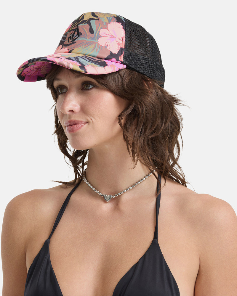 A woman in a black bikini top, silver heart necklace, and the Volcom Women's Into Paradise Hat with a floral pattern and mesh back stands against a plain white background, facing slightly to the side.