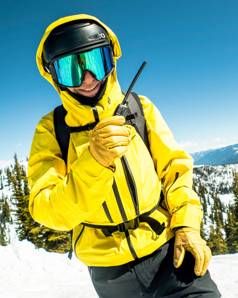 Grinning in the snowy mountains beneath a clear blue sky, this person wears the Volcom Men’s TDS® Infrared Gore-Tex Jacket—a bright yellow choice crafted from recycled nylon—with reflective goggles and a walkie-talkie in hand.