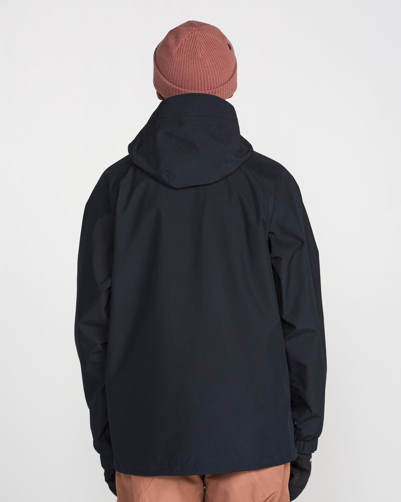 A person is seen from behind, standing against a plain white background wearing the Volcom Men’s Dua Insulated GORE-TEX Jacket in black, paired with a brown beanie and brown pants.