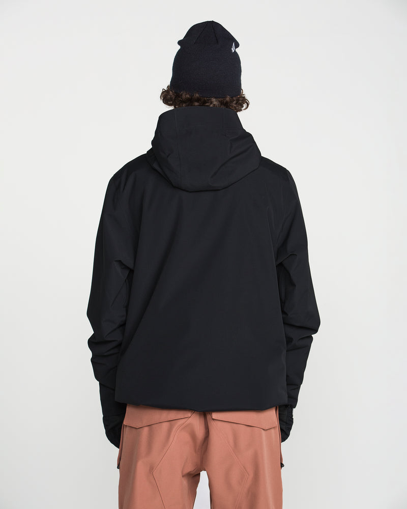 A person wearing the Volcom Men’s Double Insulated Jacket in black, paired with a black beanie and light brown pants, stands facing away from the camera against a plain white background.