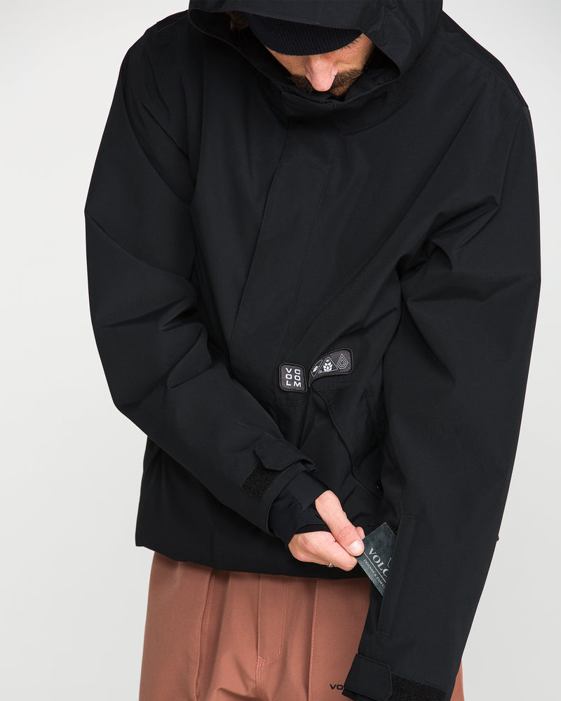 A person wearing the Volcom Men’s Double Insulated Jacket in black and brown pants unzips a pocket on the jacket’s sleeve while looking down.