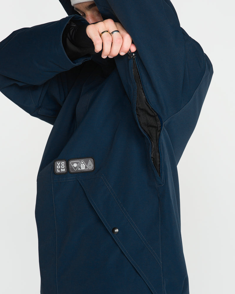 A person in the Volcom Men’s Double Insulated Jacket uses their left hand to unzip a vent under their right arm. Designed with recycled warmth in mind, the jacket features a chest patch displaying logos and a snap button pocket. The face is mostly covered.