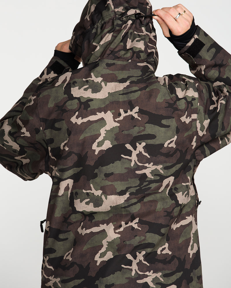A person wearing the Volcom Men’s Double Insulated Jacket, featuring a 10K/10K V-Science camouflage pattern, stands facing away from the camera with the hood up and adjusts it with both hands.