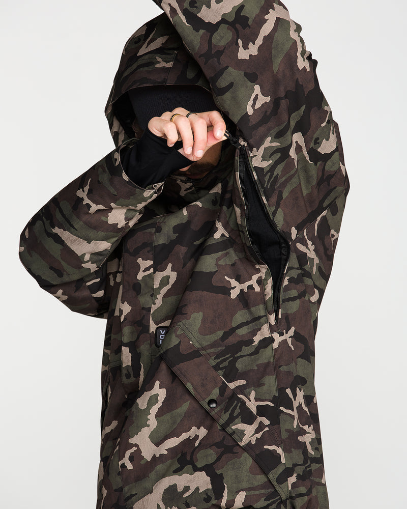 A person wearing the Volcom Men’s Double Insulated Jacket, featuring a camouflage pattern and hood, partially covers their face with their arm while adjusting the zipper. This 10K/10K V-Science layer delivers recycled warmth against a plain, light-colored background.