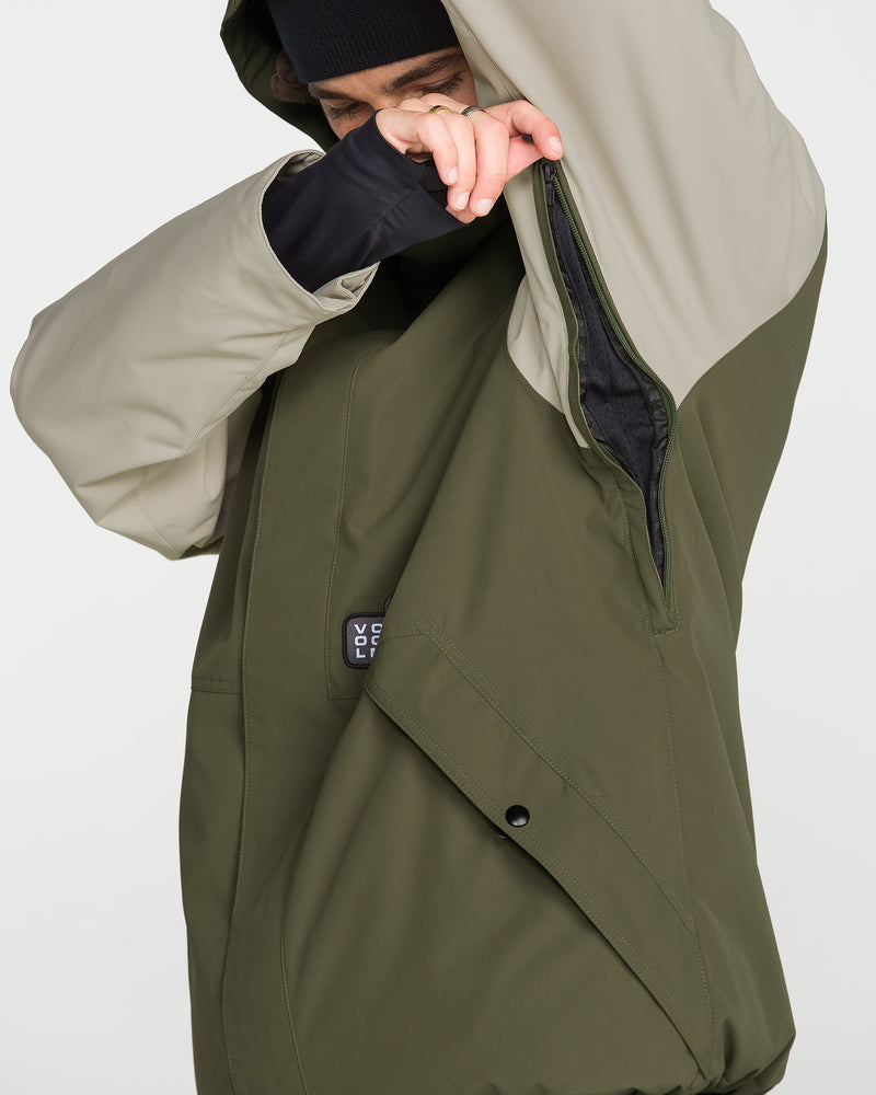 A person wearing the Volcom Men’s Double Insulated Jacket in olive and beige lifts their arm to reveal a zippered underarm vent. With only part of their face visible and a black hat on, they highlight the jacket’s Zip Tech jacket-to-pant connection for added versatility.