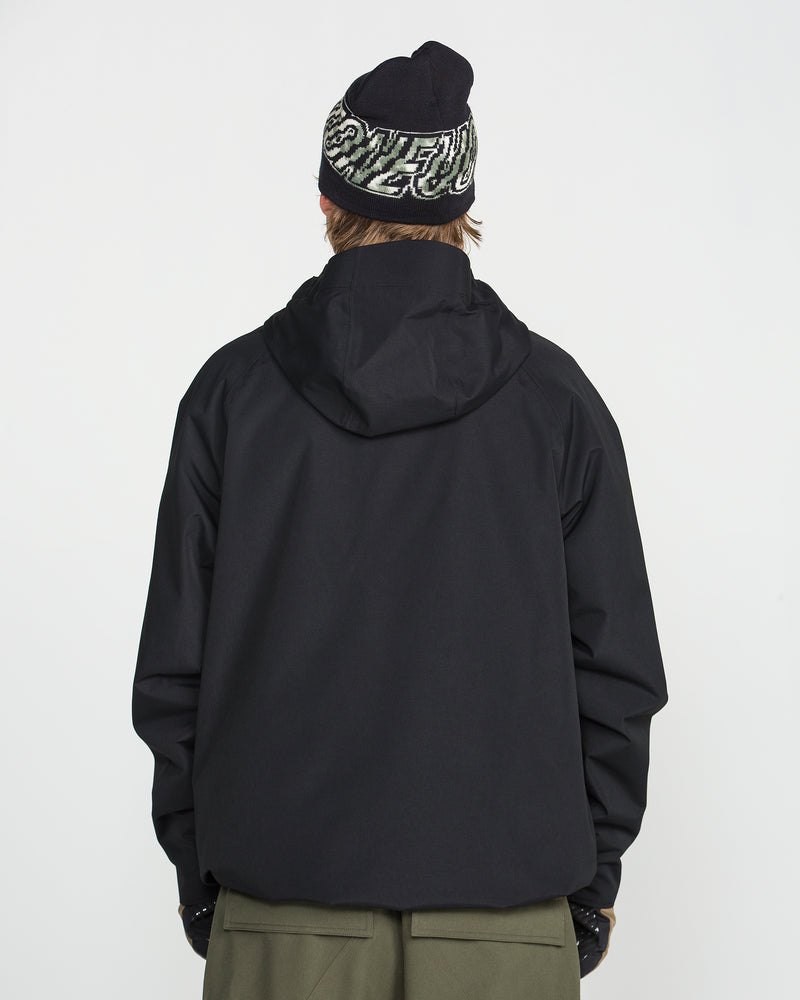 A person is shown from the back, wearing the Volcom Men’s 2836 Insulated Jacket in black, paired with olive green pants and a black beanie featuring white and green text. The background is plain white.
