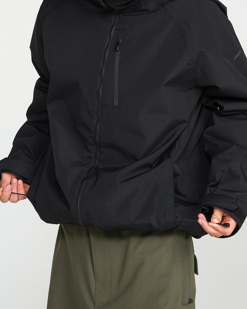 A person is wearing the Volcom Men’s 2836 Insulated Jacket in black, featuring a chest zipper pocket, paired with olive green pants. They are standing against a plain background with their head out of frame and hands partially visible.