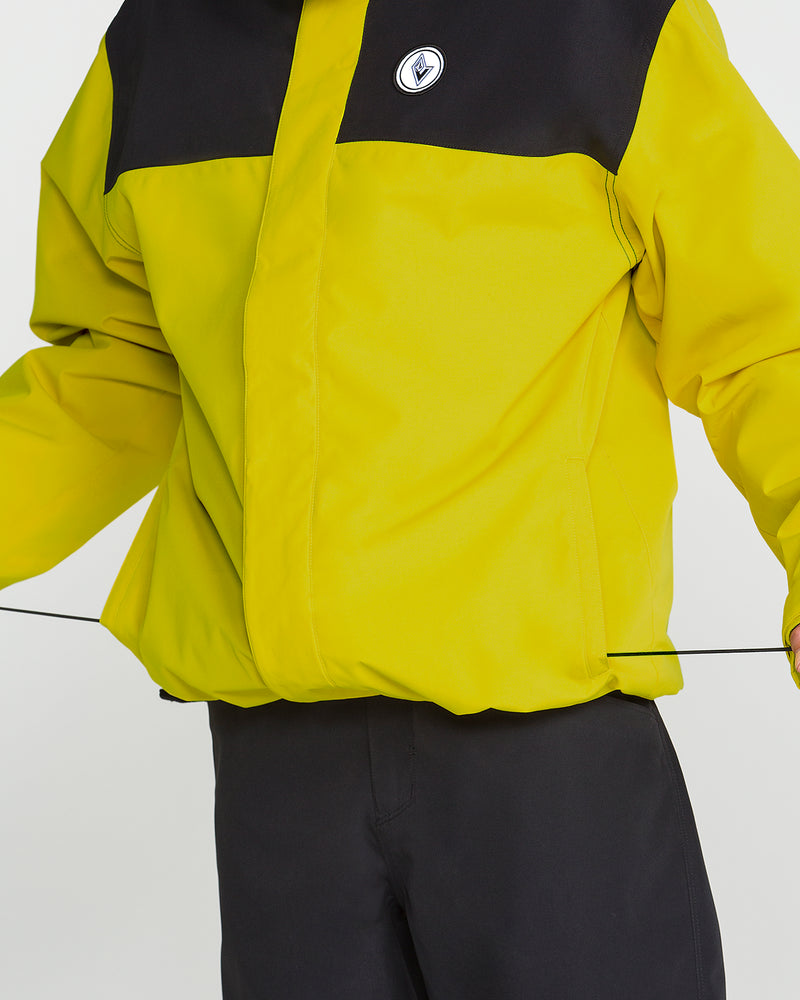 A man wearing the Volcom Men’s Buckthreeeighty Insulated Jacket in yellow and black, featuring 10K protection and a chest logo, is shown from shoulders to waist adjusting the hem drawstring; black pants are also visible.