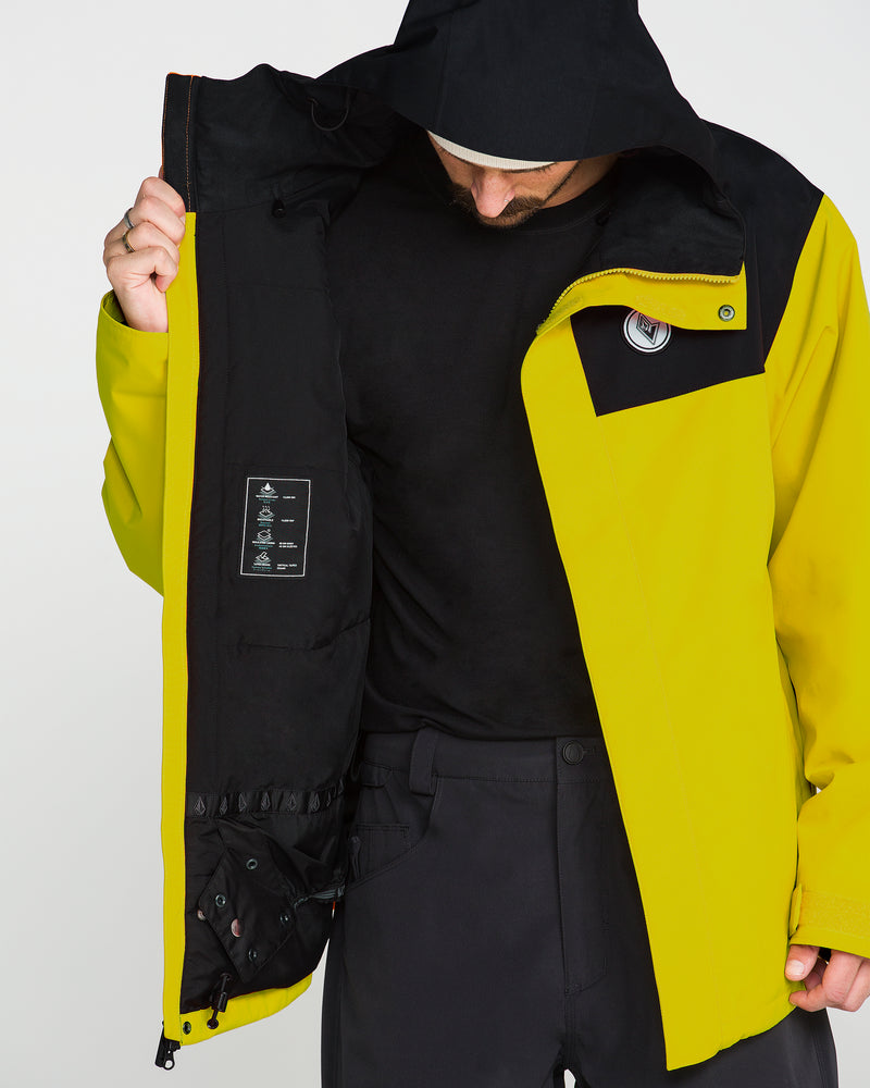 A person wearing the Volcom Men’s Buckthreeeighty Insulated Jacket in yellow and black pulls one side open to display the interior labels and pockets, crafted from recycled fabric. With their head slightly bowed and face partially hidden by the hood, the thoughtful design and 10K protection of this jacket are emphasized.