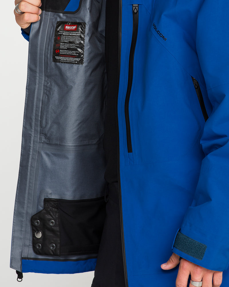 A person holds open the Volcom Men’s Guch 3L Gore-Tex Pro Jacket in blue, revealing its gray inner lining, black pocket, snap closures, and a RECCO reflector label sewn inside—features designed to offer comfort and protection while exploring the backcountry.