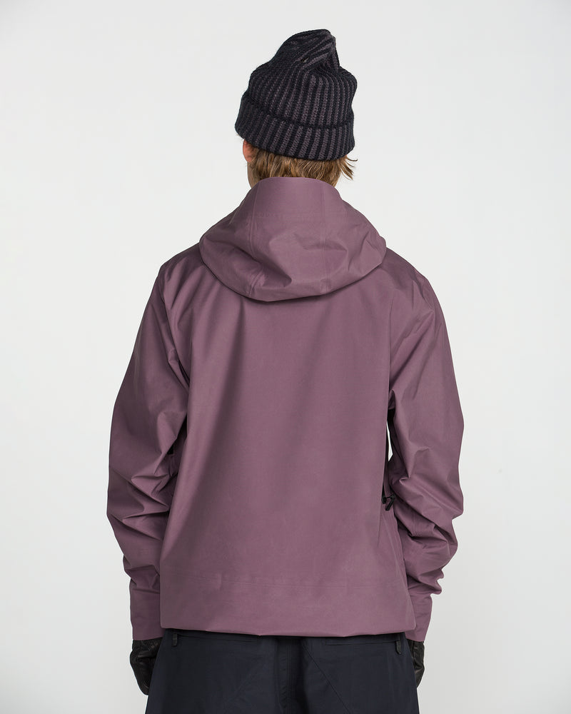 A person wearing the Volcom Unisex Tester 3L Gore-Tex Jacket in purple and a black knit beanie stands facing away from the camera against a plain white background.