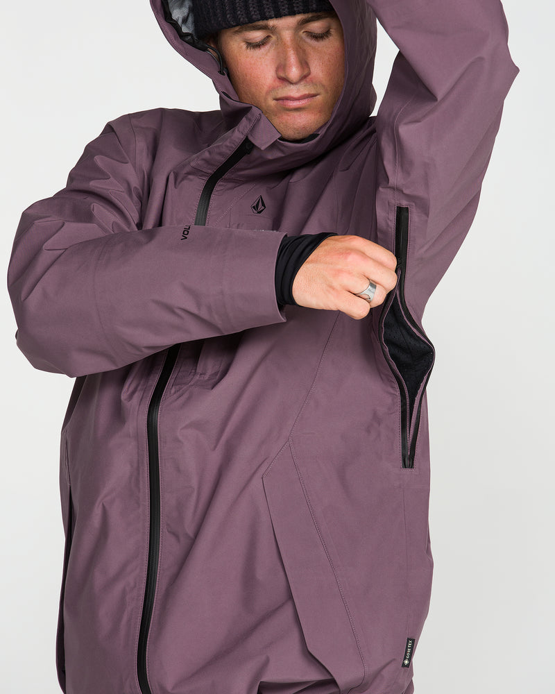 Wearing a black beanie and looking down, a person unzips the underarm ventilation on the Volcom Unisex Tester 3L Gore-Tex Jacket in purple, which is crafted from recycled three-layer fabric.
