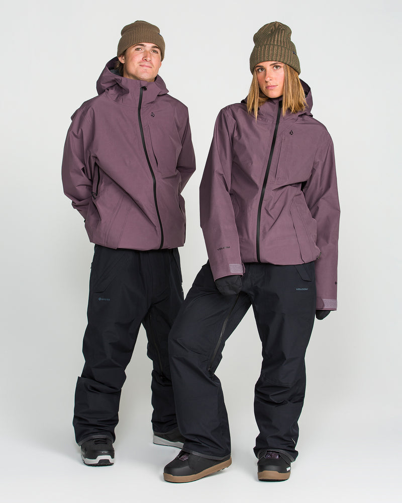 Two people stand together wearing matching Volcom Unisex Tester 3L Gore-Tex Jackets, crafted from recycled 3-layer fabric. They pair the mauve jackets with black pants, brown beanies, and winter boots, posing with neutral expressions against a plain white background.