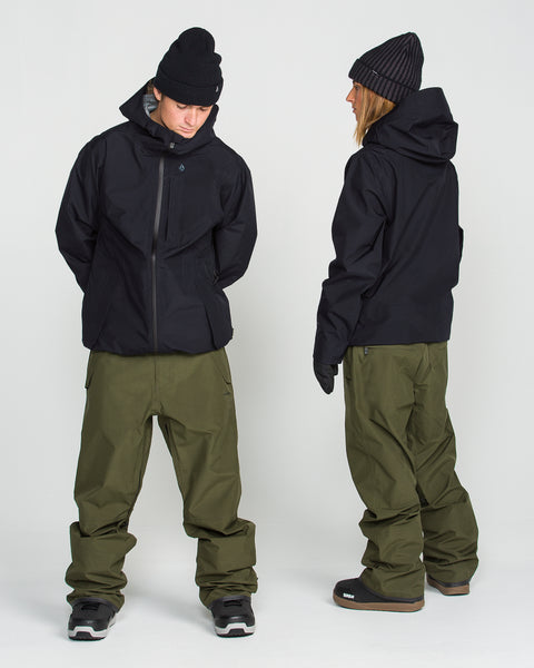 Two people wear Volcom Unisex Tester 3L Gore-Tex Jackets, paired with olive green pants and black beanies, standing against a plain white background. One person faces forward with head down, while the other stands in profile. Both are outfitted with black gloves and snow boots; their Volcom GORE-TEX shell outerwear is fully PFAS-free for mindful protection from the elements.