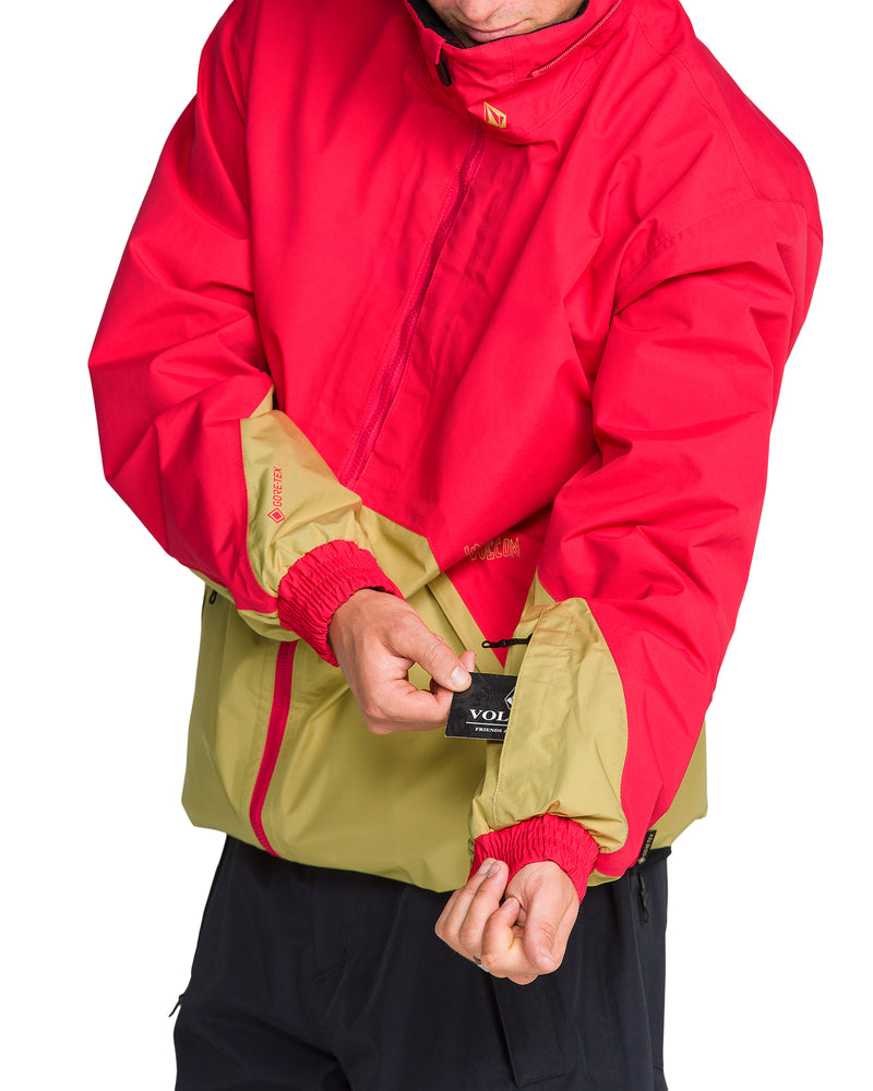 A person wearing a red and tan Men’s Longo Gore-Tex Jacket pulls a small tag out from a zippered sleeve pocket.