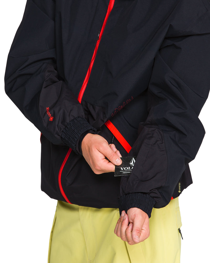 A person wearing a black recycled 2-layer Men’s Longo Gore-Tex Jacket with red zippers holds up a black brand tag attached to the sleeve.
