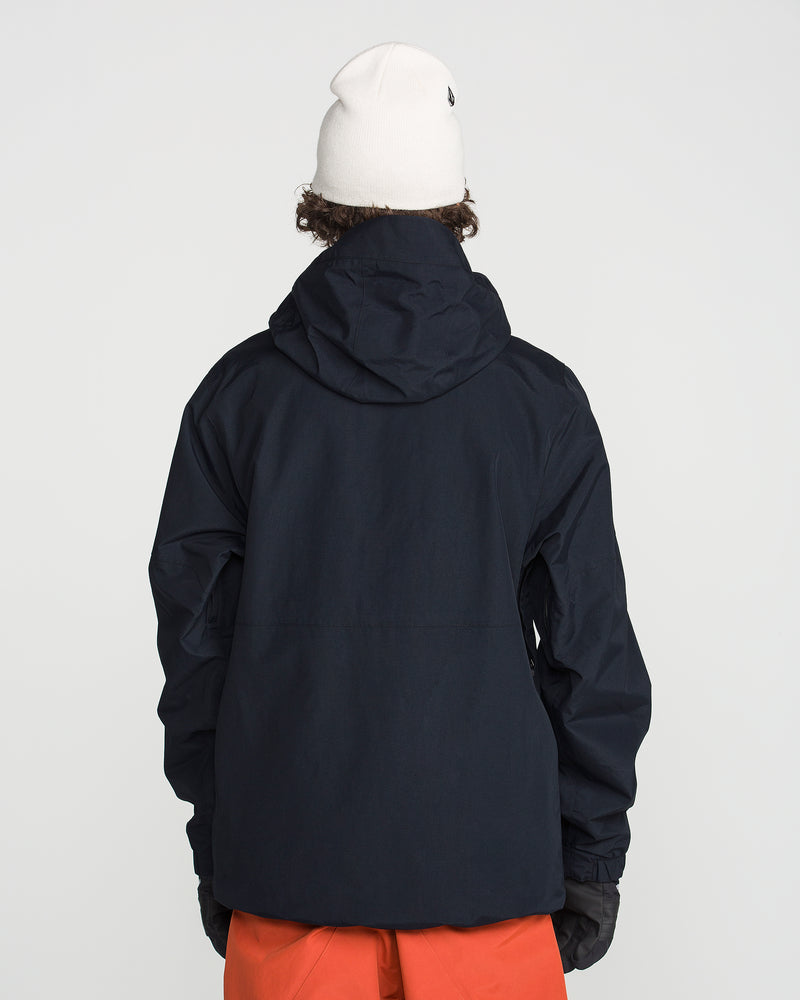 A person with curly hair is seen from behind, wearing a white beanie, black gloves, orange pants, and the Volcom Men’s L Gore-Tex Jacket—a dark hooded jacket—set against a plain light background.