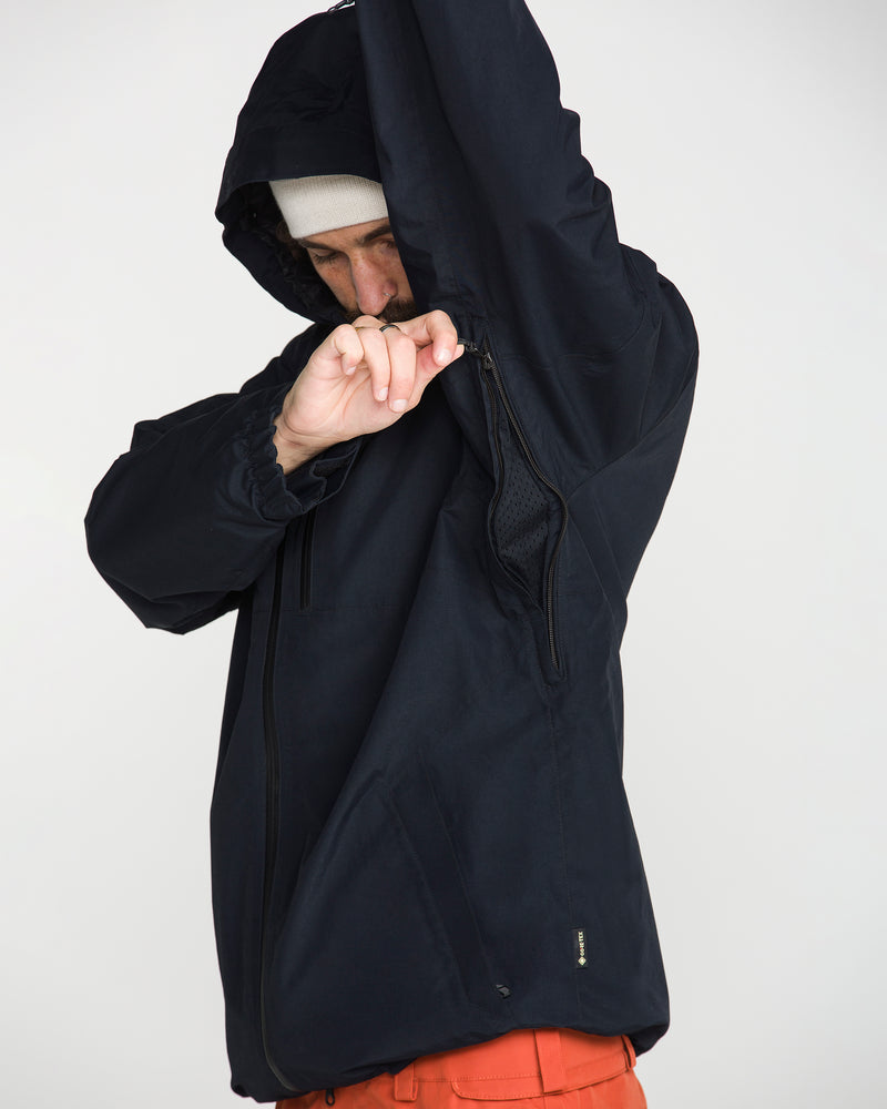 Wearing a Volcom Men’s L Gore-Tex Jacket and a white beanie, a person lifts their arm to open the zippered underarm vent, revealing mesh lining inside the waterproof jacket.