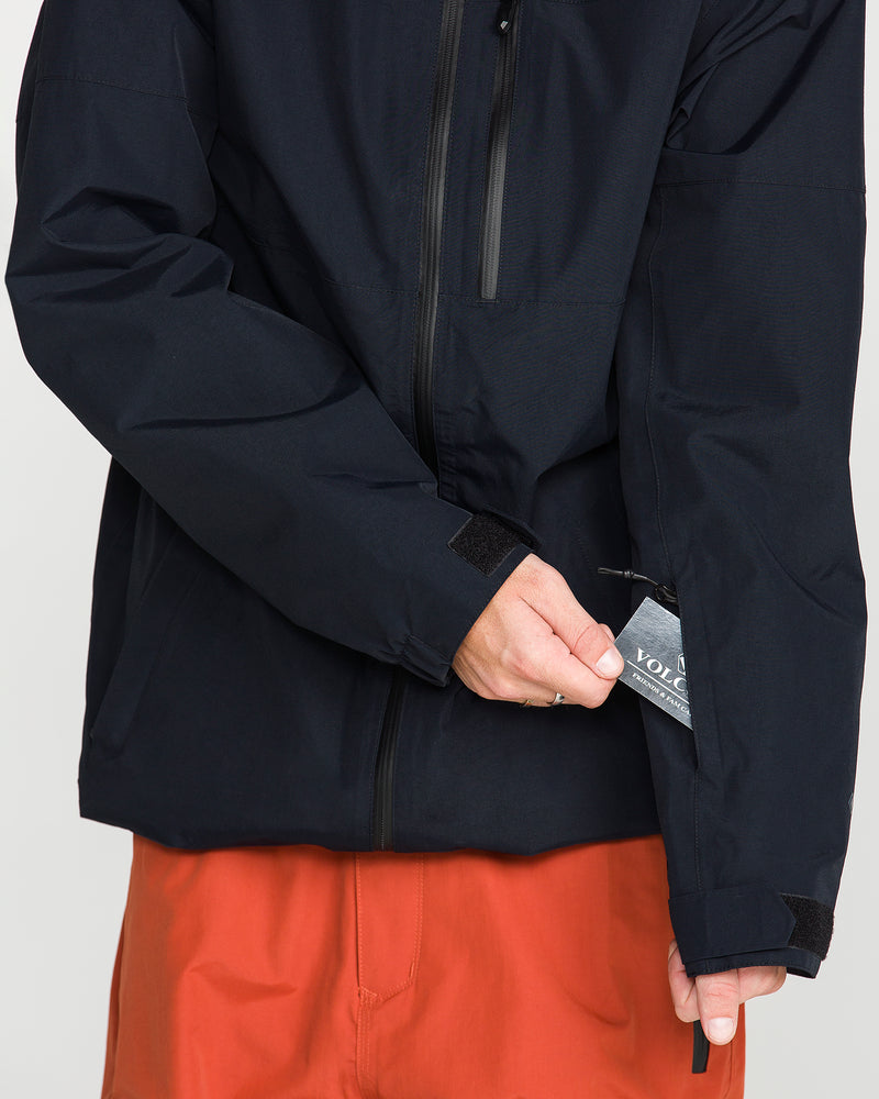 Wearing the Volcom Men’s L Gore-Tex Jacket, which features a recycled shell, someone in orange pants slips a card into the small zippered sleeve pocket on the jacket’s left arm.