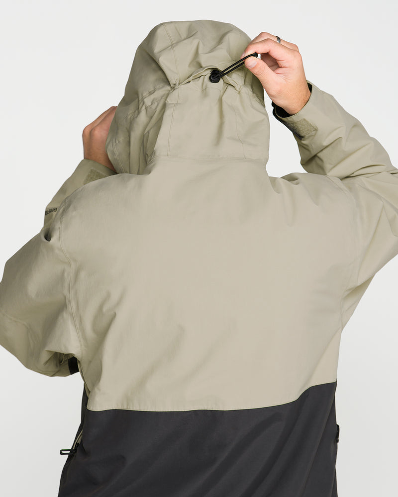 A person seen from behind adjusts the drawstring on the hood of a beige and black Volcom Men’s L Gore-Tex Jacket, crafted from recycled nylon.