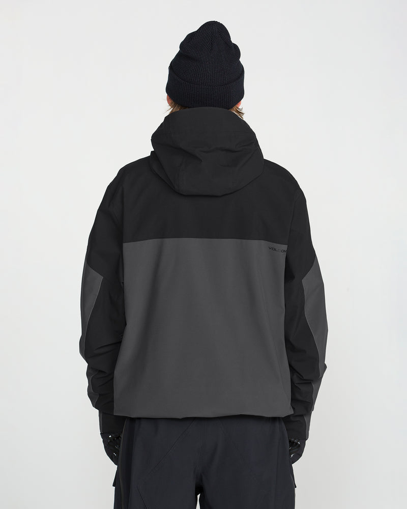 A person wearing a black beanie and the Volcom Men’s Rnge Stretch 30K Jacket in a two-tone black and dark gray colorway, crafted from recycled polyester, stands facing away from the camera against a plain white background.
