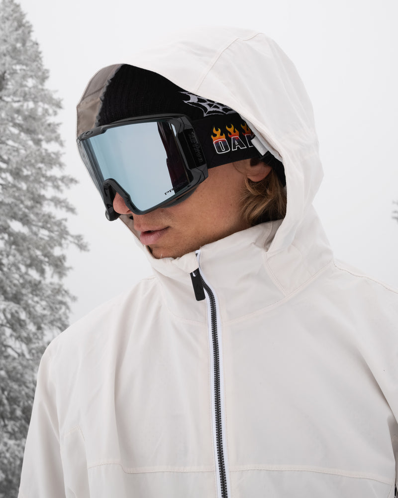 A person is wearing the Volcom Men’s Rnge Stretch 30K Jacket in white, paired with black ski goggles and a black beanie, standing outdoors in a snowy landscape with frosted trees visible in the background.
