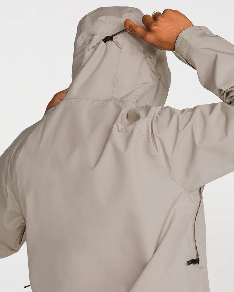 A person, seen from behind against a plain white background, adjusts the hood of a light gray Volcom Men’s Dua Gore-Tex Jacket, designed with GORE-TEX for superior waterproof protection.