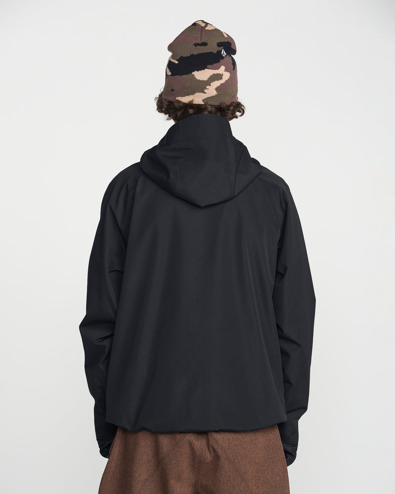 A person stands with their back to the camera, wearing the Volcom Men’s Collins 20K Jacket—a black waterproof jacket featuring a recycled shell—paired with brown pants and a camouflage beanie. The background is plain white.