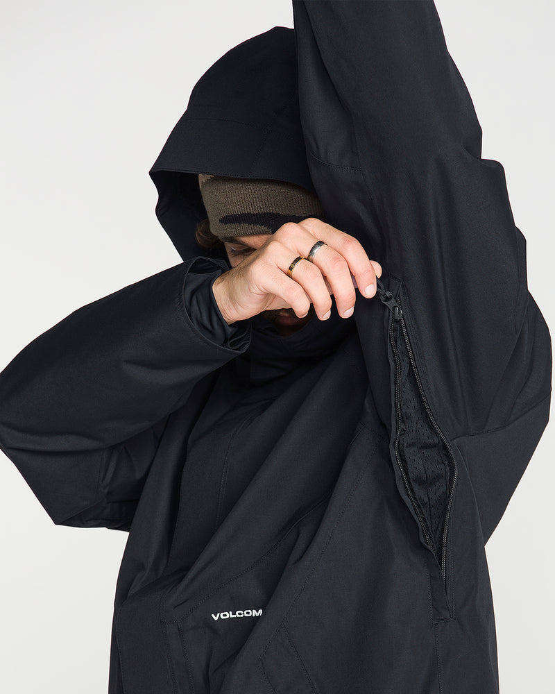 A person wearing the Volcom Men’s Collins 20K Jacket in black, featuring a waterproof shell and hood, unzips the underarm vent to show the recycled lining inside. Only part of their face is in view. They are also wearing a brown beanie and have a ring on one finger.