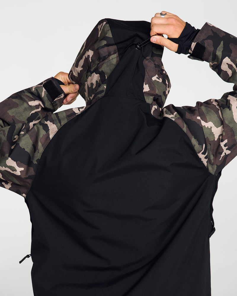 A person seen from behind pulls up the hood on a camouflage and black Volcom Men’s Collins 20K Jacket, their face hidden.
