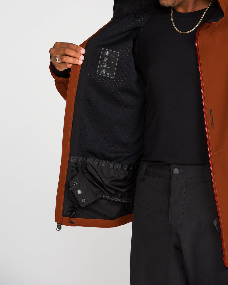 A person wearing black pants and a dark shirt displays the interior of the Volcom Men’s Brighton Full Zip Jacket, highlighting its black mesh lining, inner label, and innovative Zip Tech jacket-to-pant interface. The individual’s face is not visible.