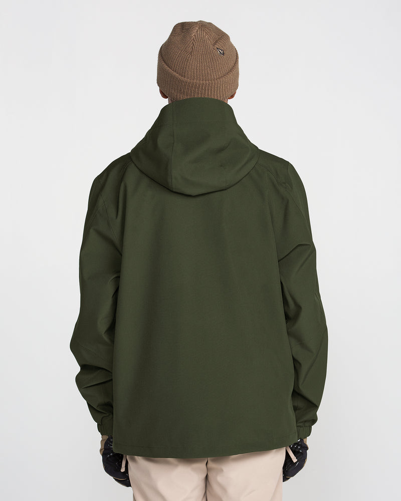 A person wearing a brown beanie, beige pants, black gloves, and the Volcom Men’s Brighton Full Zip Jacket in dark green recycled stretch material with fully taped seams is standing with their back facing the camera against a plain white background.