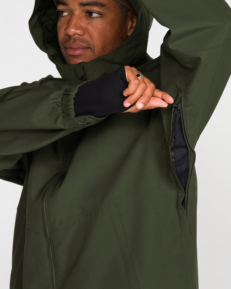 A man wearing the Volcom Men’s Brighton Full Zip Jacket in dark green opens a zippered underarm vent, revealing a mesh lining inside. With his left arm raised and his face partially visible as he looks to the side, the jacket’s fully taped seams underscore its enhanced protection against the elements.