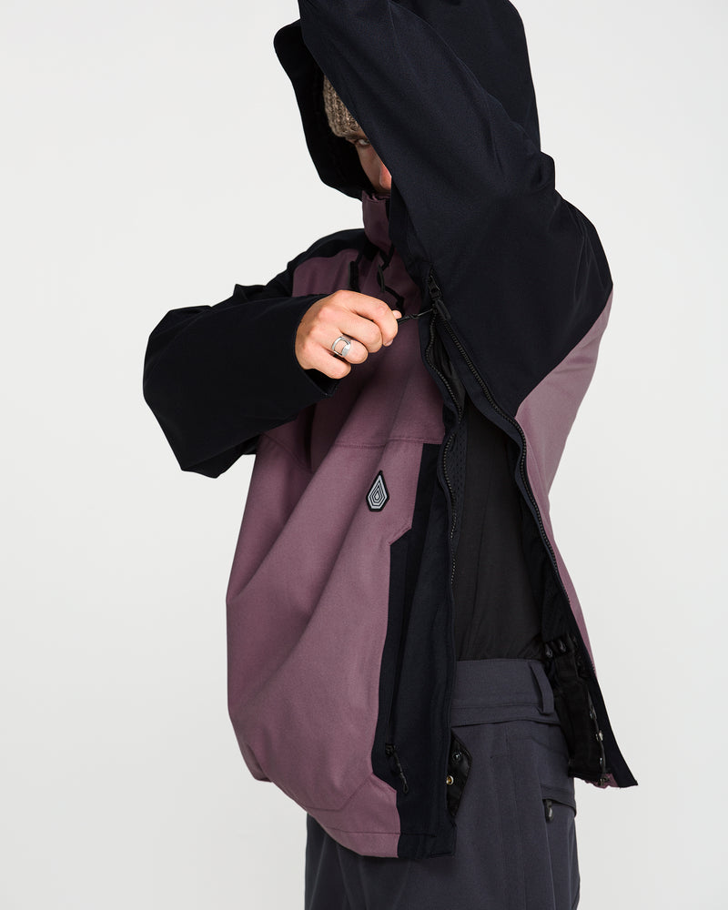 A person wearing the Volcom Men’s Hossegor 20K Pullover in purple and black unzips a side vent, their face partly hidden by the hood and arm. This 20K pullover features a small Volcom logo on the chest.