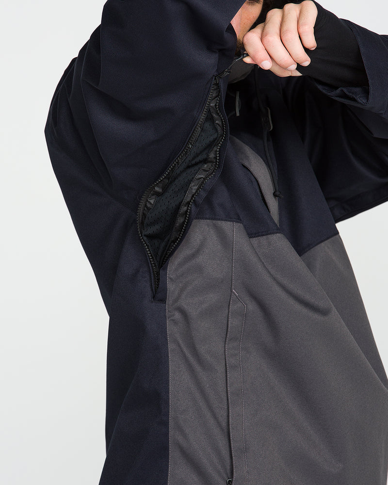 A person unzips an underarm ventilation zipper on a dark-colored Volcom Men’s Hossegor 20K Pullover, exposing a mesh lining made from recycled V-Science shell fabric. The individual’s face is not visible.