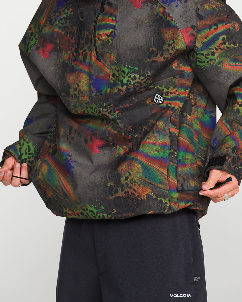 A person wears the Volcom Men’s Hossegor 20K Pullover—an oversized jacket showcasing a vibrant, abstract design and constructed from recycled V-Science shell with PFAS-free DWR. Black pants adorned with a small Volcom logo complete the look. Only the torso and part of the arms are visible; the individual’s face remains out of frame.