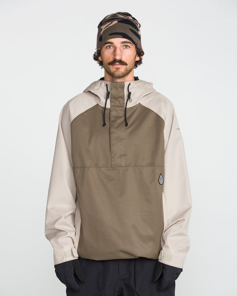 A man with a mustache wears the Volcom Men’s Hossegor 20K Pullover—a two-tone hooded jacket made from recycled V-Science shell with PFAS-free DWR—paired with black gloves and a camouflage beanie, standing against a plain white background.