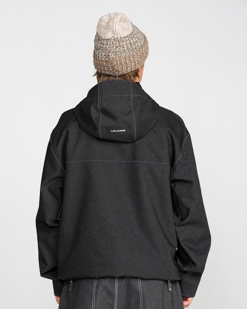 A person is shown from behind against a plain light background, wearing the Volcom Men’s Top Stitch Jacket— a black hooded 10K waterproof jacket with “VOLCOM” printed on the back— paired with a beige knit beanie.