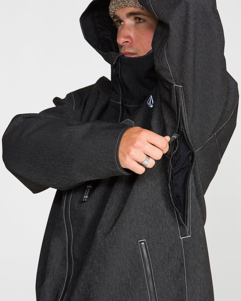 A person in a dark hooded Volcom Men’s Top Stitch Jacket unzips an underarm vent. The jacket showcases white stitching, a small Volcom logo on the chest, and provides a comfortable, baggy fit. The individual is also wearing a knit hat and a ring.