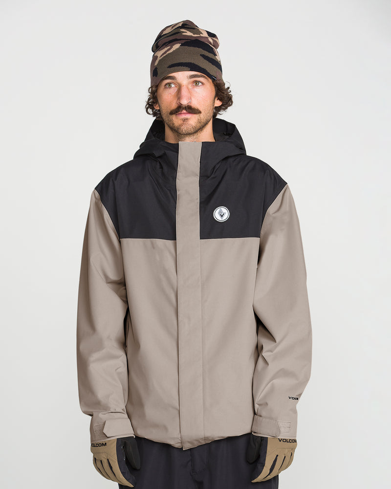 A man with a mustache wears the Volcom Men’s Buckthreeeighty Jacket, which features PFAS-free DWR, along with a patterned beanie and gloves. He stands against a plain white background, looking slightly to the side.
